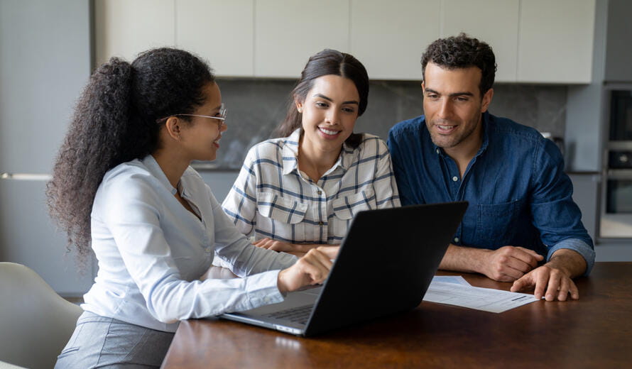 three people sitting around a laptop