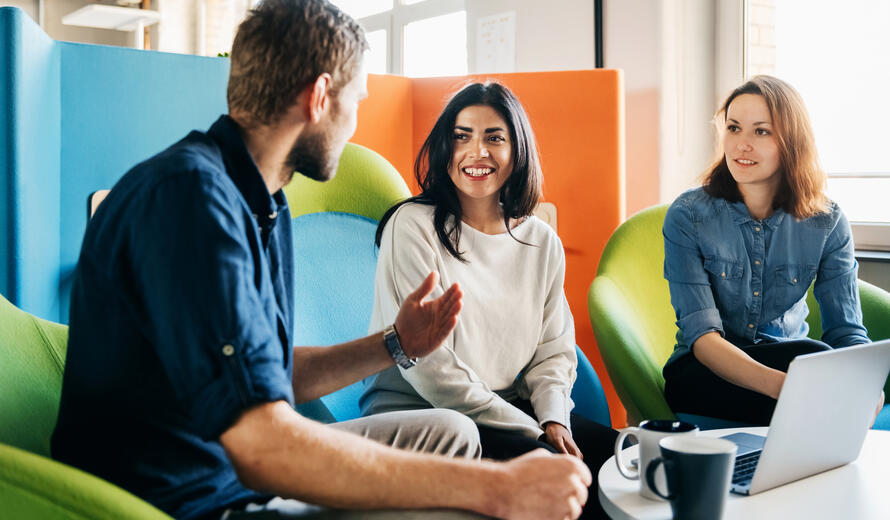 A meeting between three team leaders sitting in colorful chairs in a modern office environment.