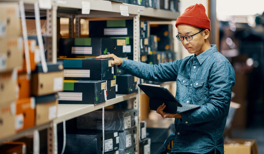 Mid adult male retail shop staff checking or looking for inventory in a storage room by using a digital tablet