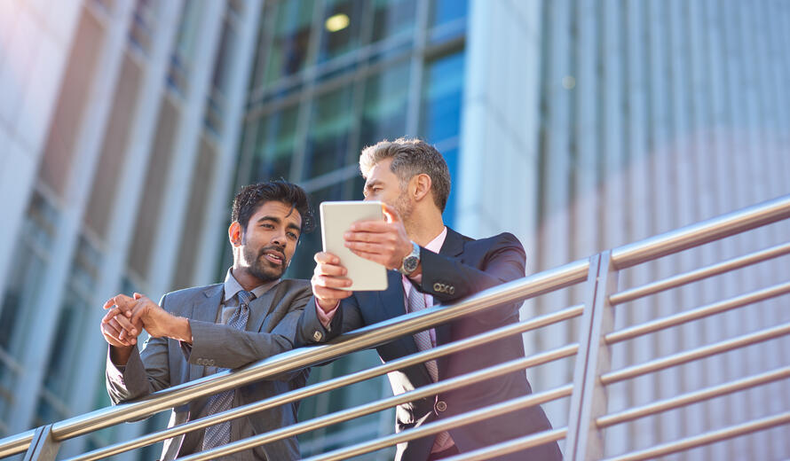 Two businessmen outside in the city discussing plans on a digital tablet.